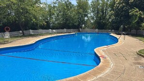 Une piscine aux bords incurvés, entourée d’une clôture blanche, avec des arbres en arrière-plan.