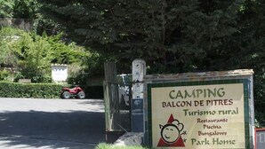 Un panneau indiquant un terrain de camping appelé « Balcon de Pitres », qui propose des commodités telles qu’un restaurant, une piscine, des bungalows et des logements de type « parc résidentiel ».