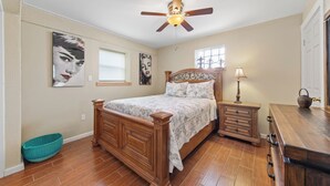 A bedroom with a wooden bed, a nightstand, a lamp, and a ceiling fan. - Spacious Beach House w/Fenced Yard, Firepit, Patio & Walk to Beach! (South Padre Island)