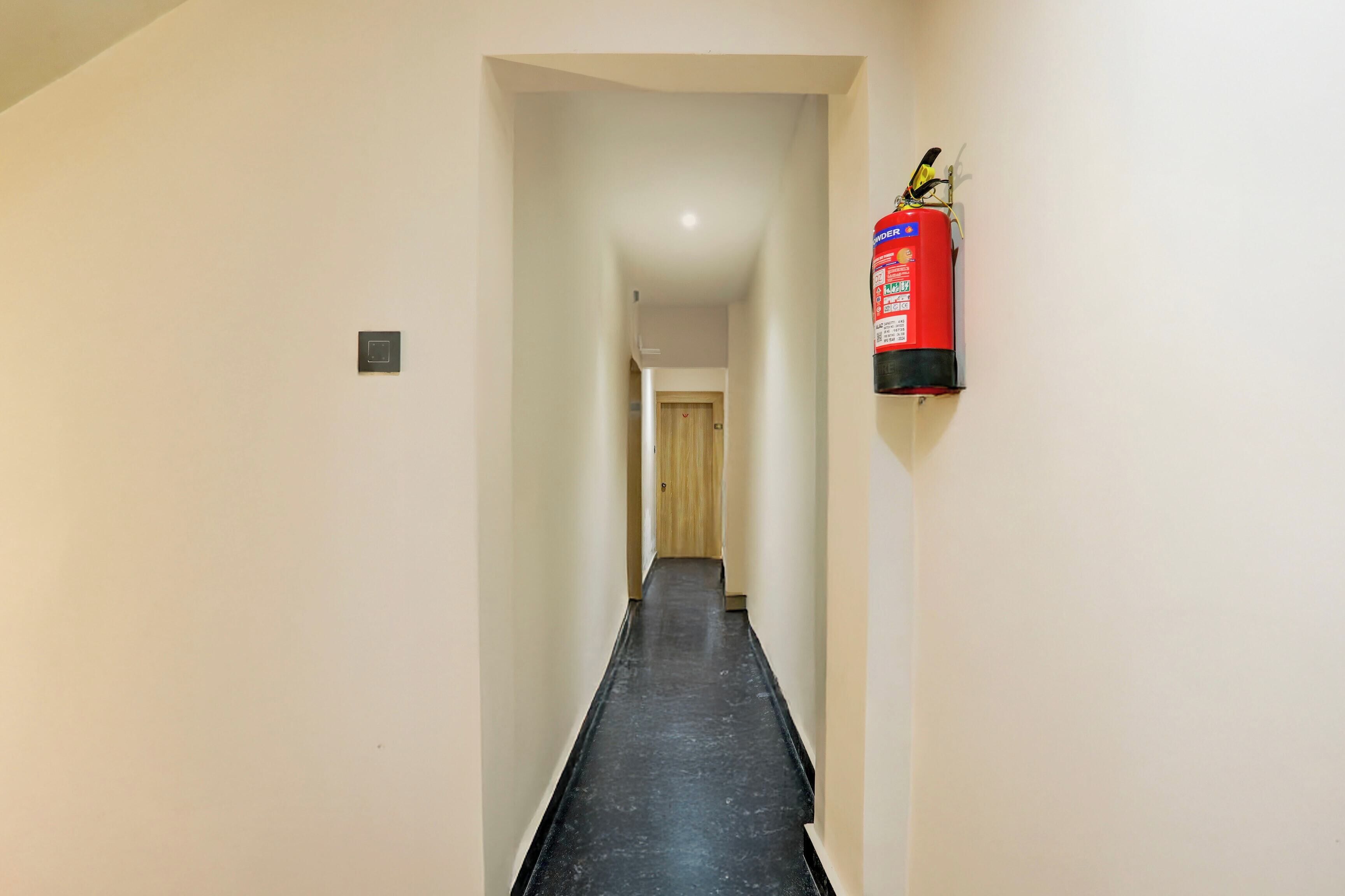 Un pasillo estrecho con un extintor colgado en la pared, una puerta al final y un interruptor de luz en la pared.