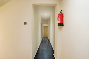 A narrow hallway with a fire extinguisher mounted on the wall, a door at the end, and a light switch on the wall.