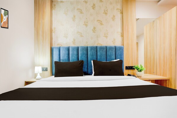 A modern hotel room with a large bed, a blue headboard, and a nightstand with a lamp and phone.