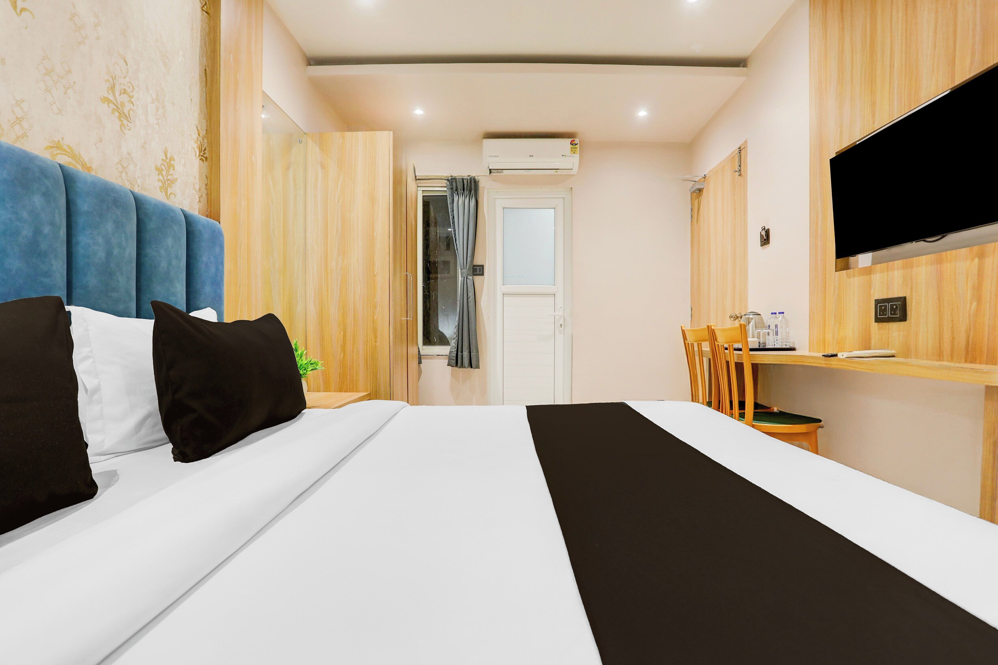 Quarto de hotel com uma cama, uma escrivaninha, uma cadeira, uma televisão e porta do banheiro.