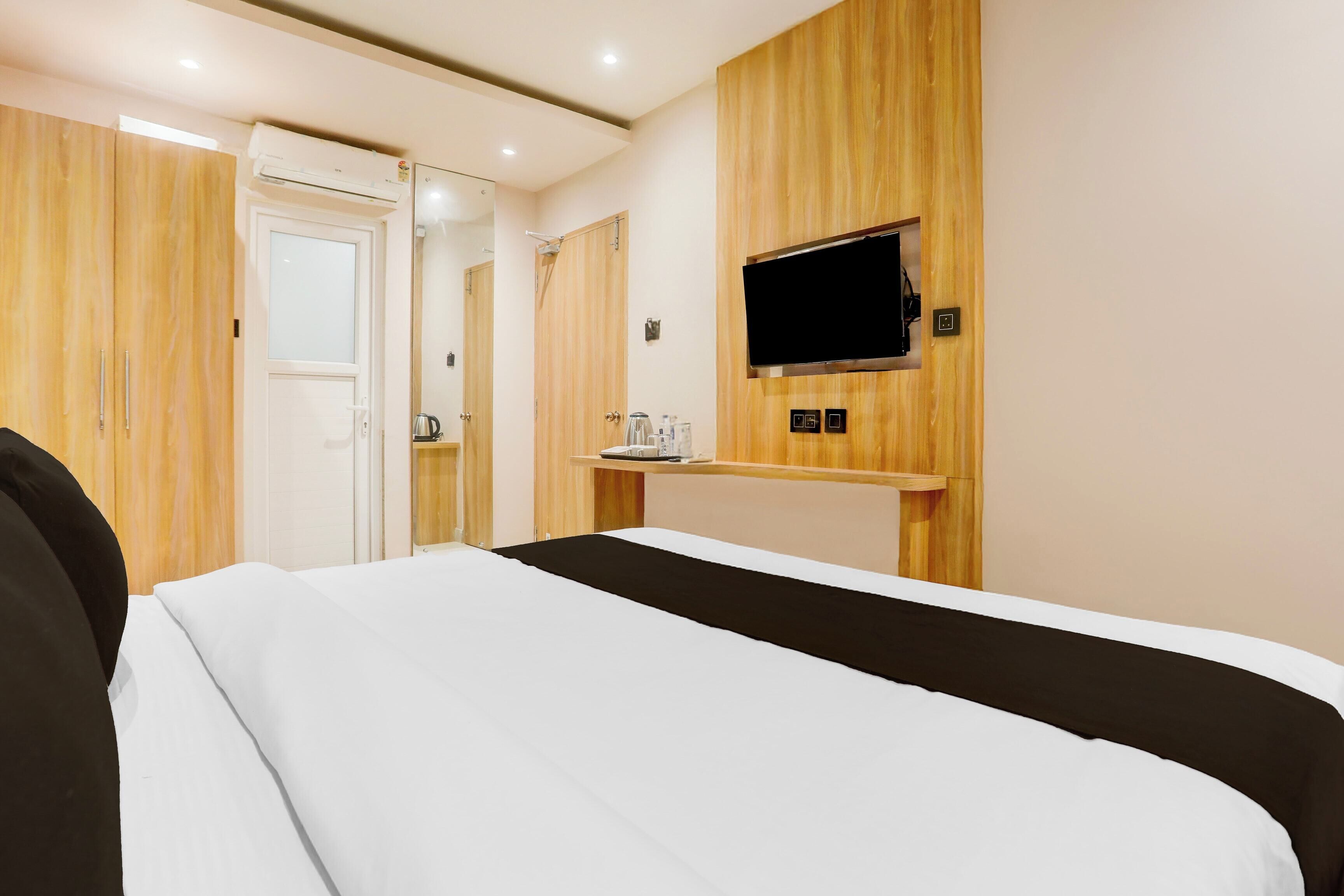 Une chambre d’hôtel avec un lit, un téléviseur fixé au mur et une petite table avec une bouilloire.