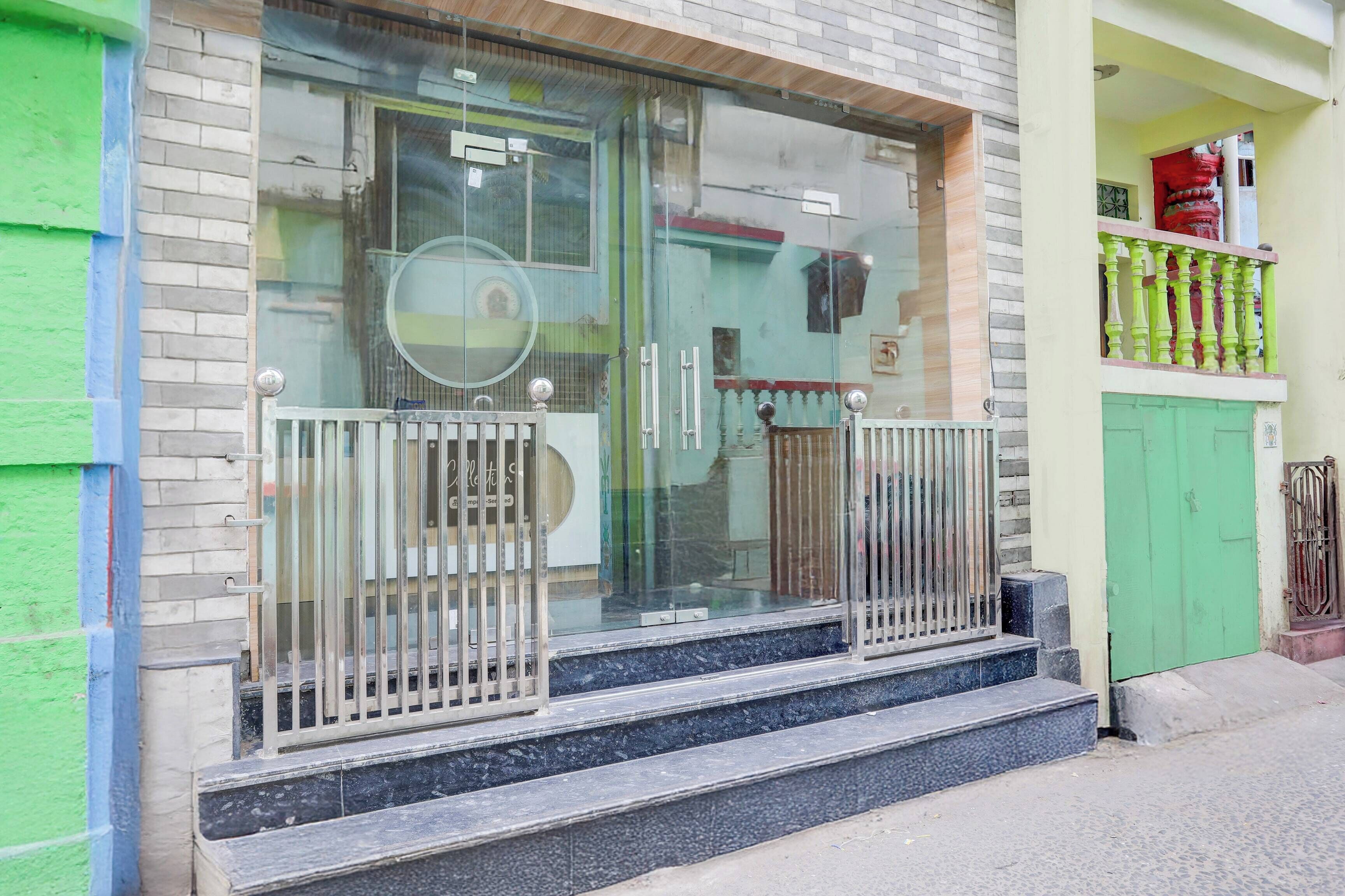 Un edificio con entrada de vidrio, barandillas de metal y una puerta verde.