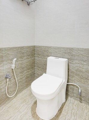 A bathroom with a toilet, a shower, and a marble-patterned wall.