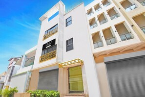 A multi-story building with a modern design, featuring balconies with metal railings, large windows, and a sign indicating a company service. - Collection O Gandhi Ghat Formerly Sai (Puri)