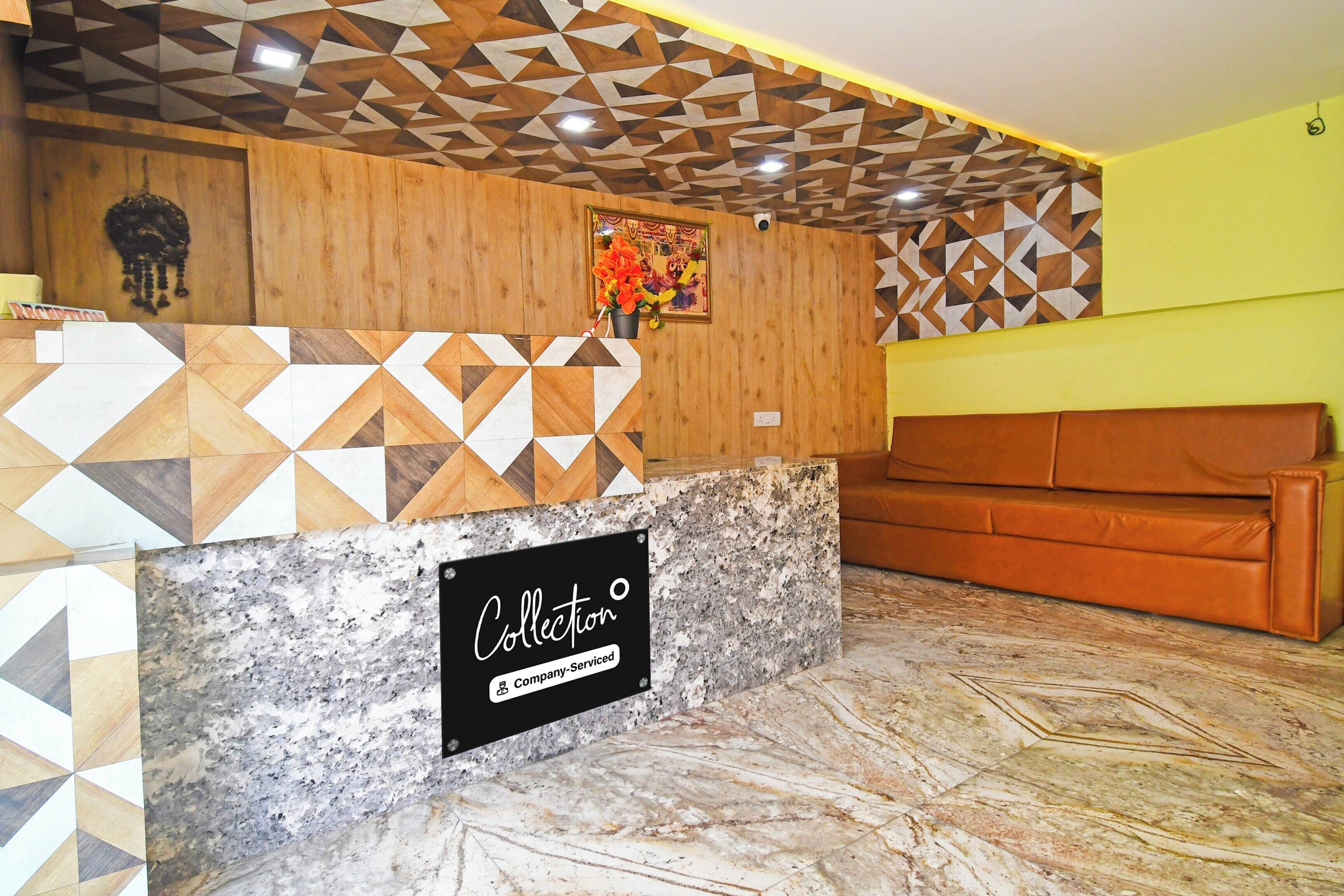 Un espace d’accueil avec un mur orné d’un motif géométrique, un comptoir en marbre et un canapé marron.