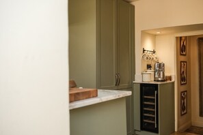 A compact kitchen with a marble countertop, a coffee machine, and a set of hanging pots. - Boutique Cotswolds Cottage near Soho Farmhouse (Duns Tew)