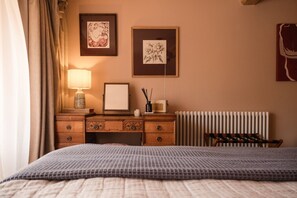 A hotel room with a bed, a wooden dresser, a lamp, two framed artworks, a radiator, and a chair. - Boutique Cotswolds Cottage near Soho Farmhouse (Duns Tew)