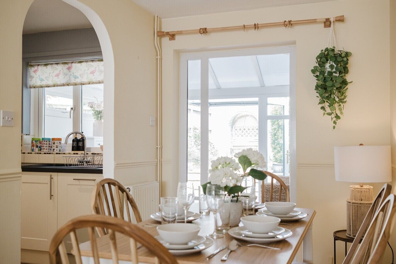 Comedor con una mesa preparada para cuatro, sillas, una planta colgante y una ventana con vistas.