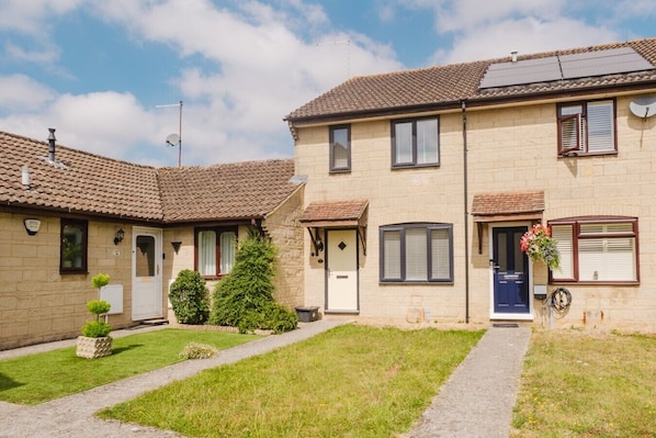 Een woonhuis met twee verdiepingen, een pannendak, een voordeur en een kleine tuin met een pad.