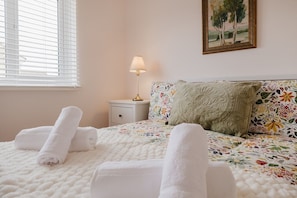 Een net opgemaakt bed met opgerolde handdoeken, een bedlampje en een sierkussen met bloemenprint.