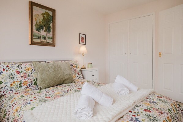 Un dormitorio con colcha estampada, almohada verde, lámpara de noche y puerta blanca.