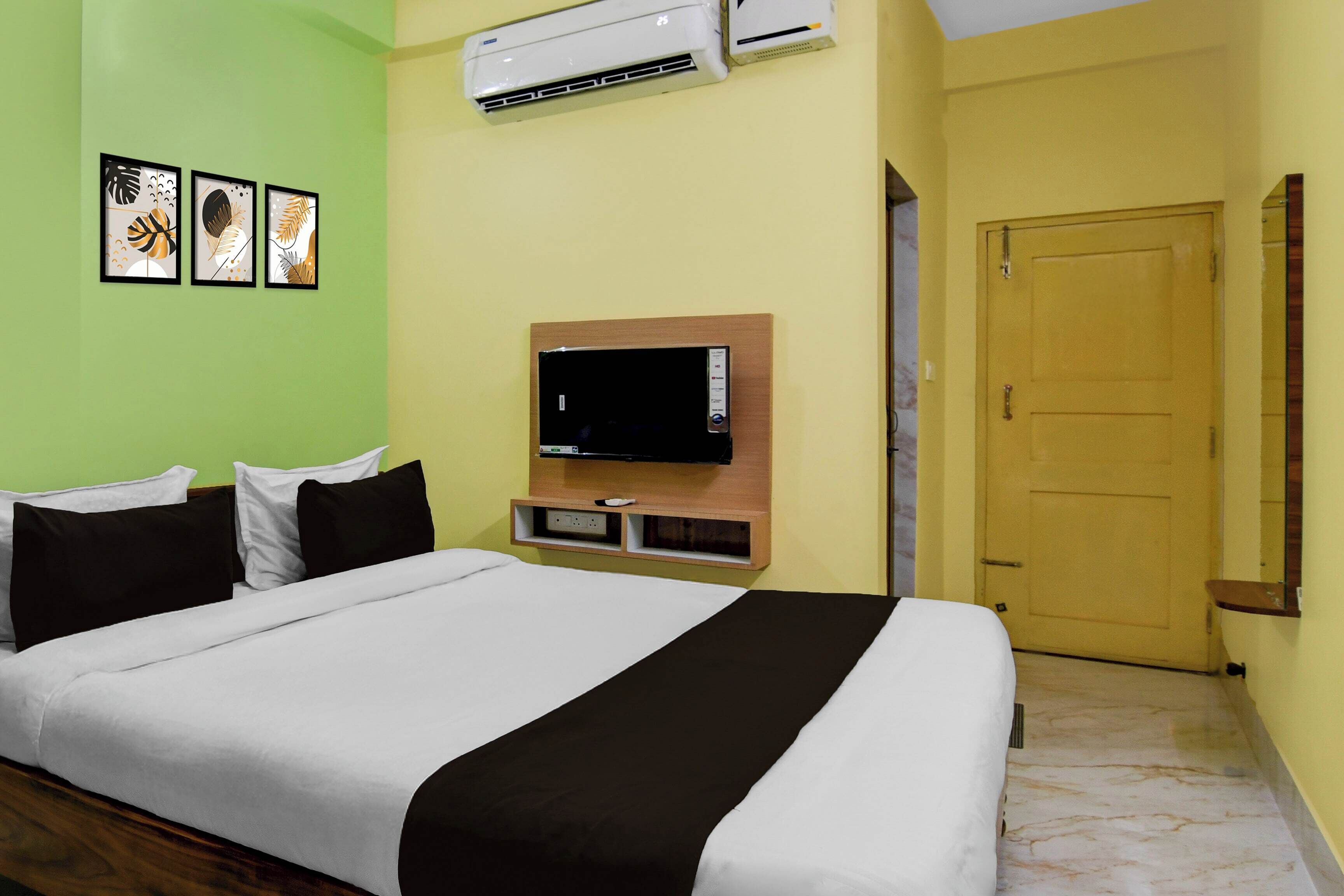 A hotel room with a bed, a mounted TV, an air conditioner, and a door.