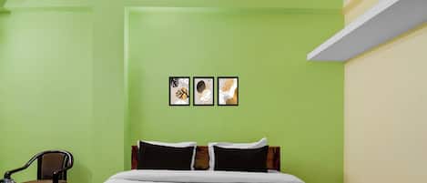Habitación de hotel con una cama, dos almohadas, una silla, una mesita con bandeja y tres cuadros enmarcados en la pared.