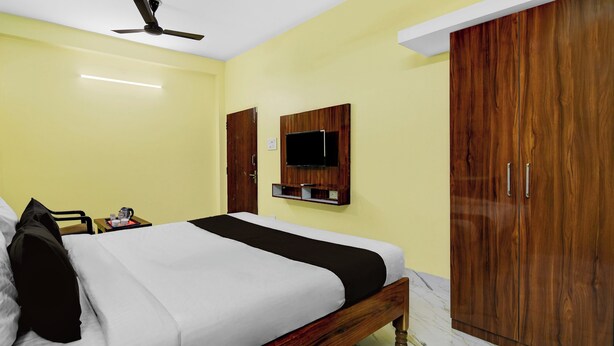 A hotel room with a bed, a wardrobe, a television mounted on the wall, and a ceiling fan. - Collection O Shree Jagannatha Temple (Puri)