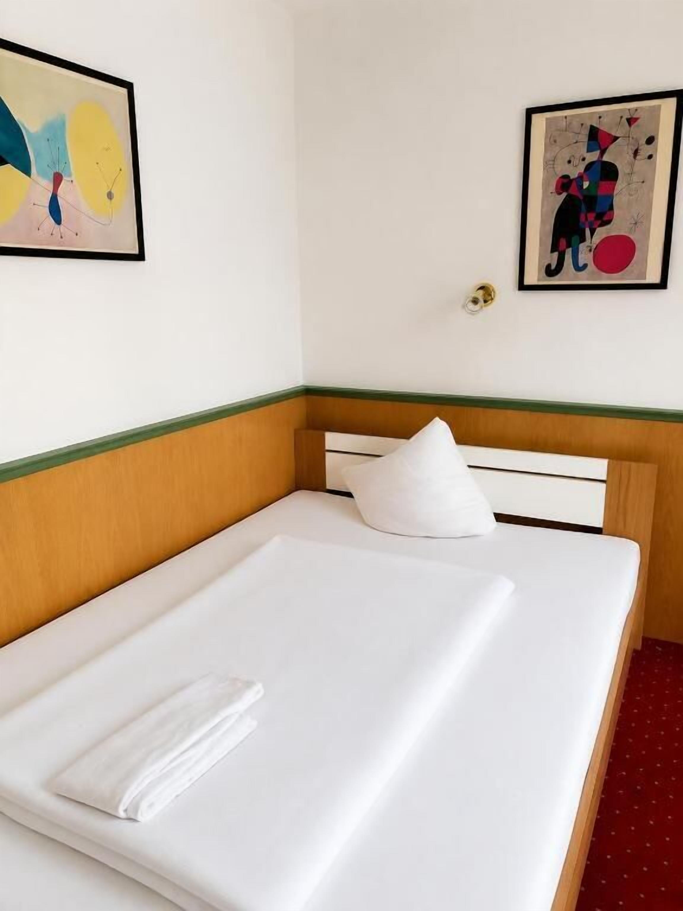 Ein Hotelzimmer mit einem ordentlich bezogenen Bett, einem Kopfkissen und zwei gerahmten Kunstwerken an den Wänden.