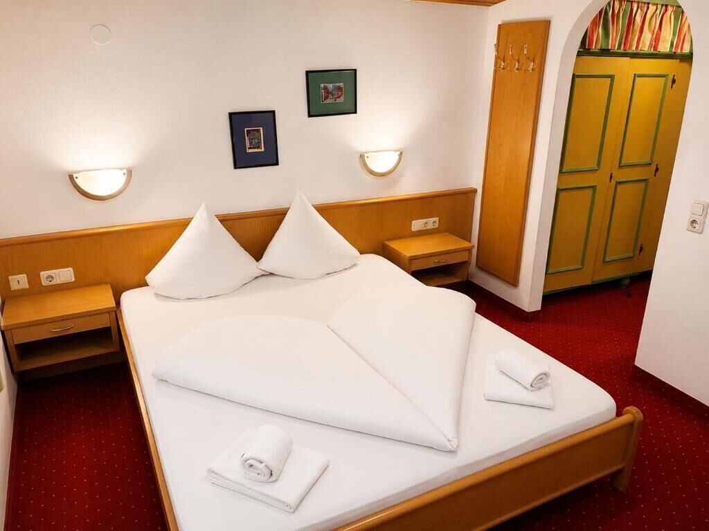 Et hotelværelse med seng, sengeborde, vægmonterede lamper, et klædeskab og et rødt tæppe.
