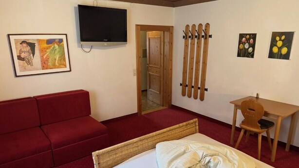 Ein Hotelzimmer mit einem Bett, einem roten Sofa, einem Fernseher und Kunstwerken an den Wänden.