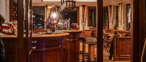 A bar area with wooden stools, a bar counter, and hanging lights.