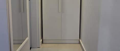 A narrow hallway with a closet and a door on the left, and a wardrobe on the right.