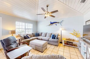 A spacious living room with a ceiling fan, a large window, a sofa set, a television, and a decorative fish mural. - 3 BR, 2 BA Pet-friendly Fort Morgan home with water views! (Gulf Shores)