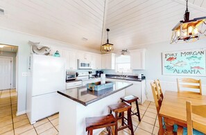A spacious kitchen with white cabinetry, a central island, and a dining area with wooden chairs. - 3 BR, 2 BA Pet-friendly Fort Morgan home with water views! (Gulf Shores)