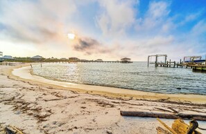 A beach with a wooden pier extending into calm waters, a clear sky, and a sunset. - 3 BR, 2 BA Pet-friendly Fort Morgan home with water views! (Gulf Shores)