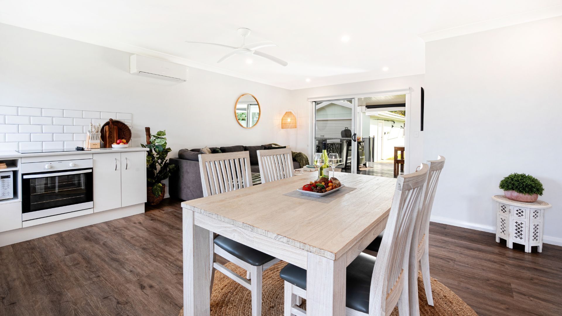 Une cuisine moderne avec des meubles blancs, un four encastré et un coin repas comprenant une table et des chaises en bois.