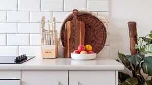 A kitchen counter with a knife block, a wooden cutting board, a woven basket, and a bowl of fruit. - Periwinkle - perfect base for a beachside getaway with family and pets (Culburra Beach)