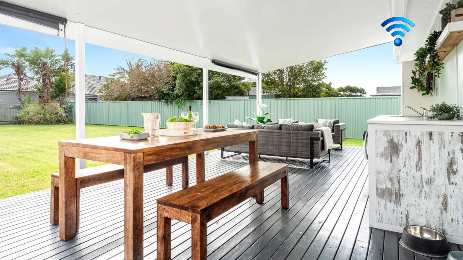 Un patio al aire libre con mesa y banco de madera, un sofá y una zona de bar.