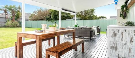 Un patio al aire libre con mesa y banco de madera, un sofá y una zona de bar.