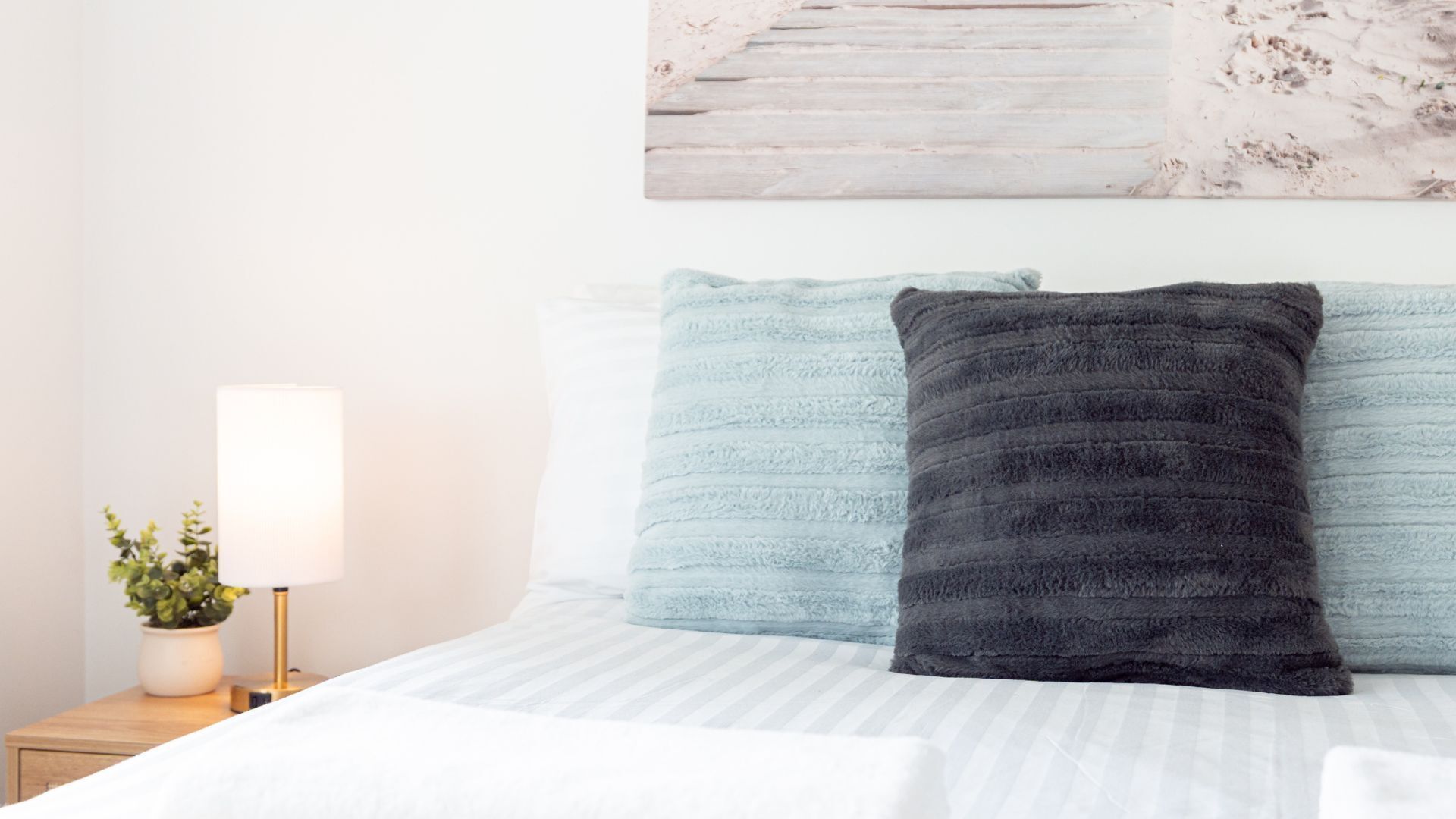 A bed with two pillows, a bedside table with a lamp, and a wall-mounted artwork.