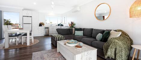 A modern living room with a grey sofa, a coffee table, and a dining area with a white table and chairs.