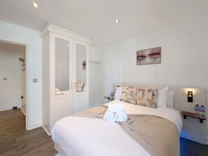 A hotel room with a bed, a wardrobe, a bedside table with a lamp, and a wall-mounted artwork. - Fully Serviced One Bed Apartment near London Excel (Greater London)