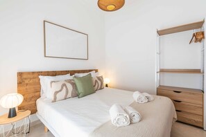 A neatly arranged bedroom with a wooden headboard, a bed with white bedding, a bedside lamp, and a hanging wardrobe. - Casa da Bica T2 250m Old Town Beach (Albufeira)