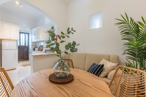 Un salon moderne avec une table ronde en bois, un vase en verre contenant des feuilles vertes, un canapé et une grande plante en pot.