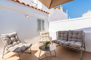 An outdoor seating area with two cushioned chairs and a small table, a potted plant, and a white wall with a window and shutters. - Casa da Bica T2 250m Old Town Beach (Albufeira)
