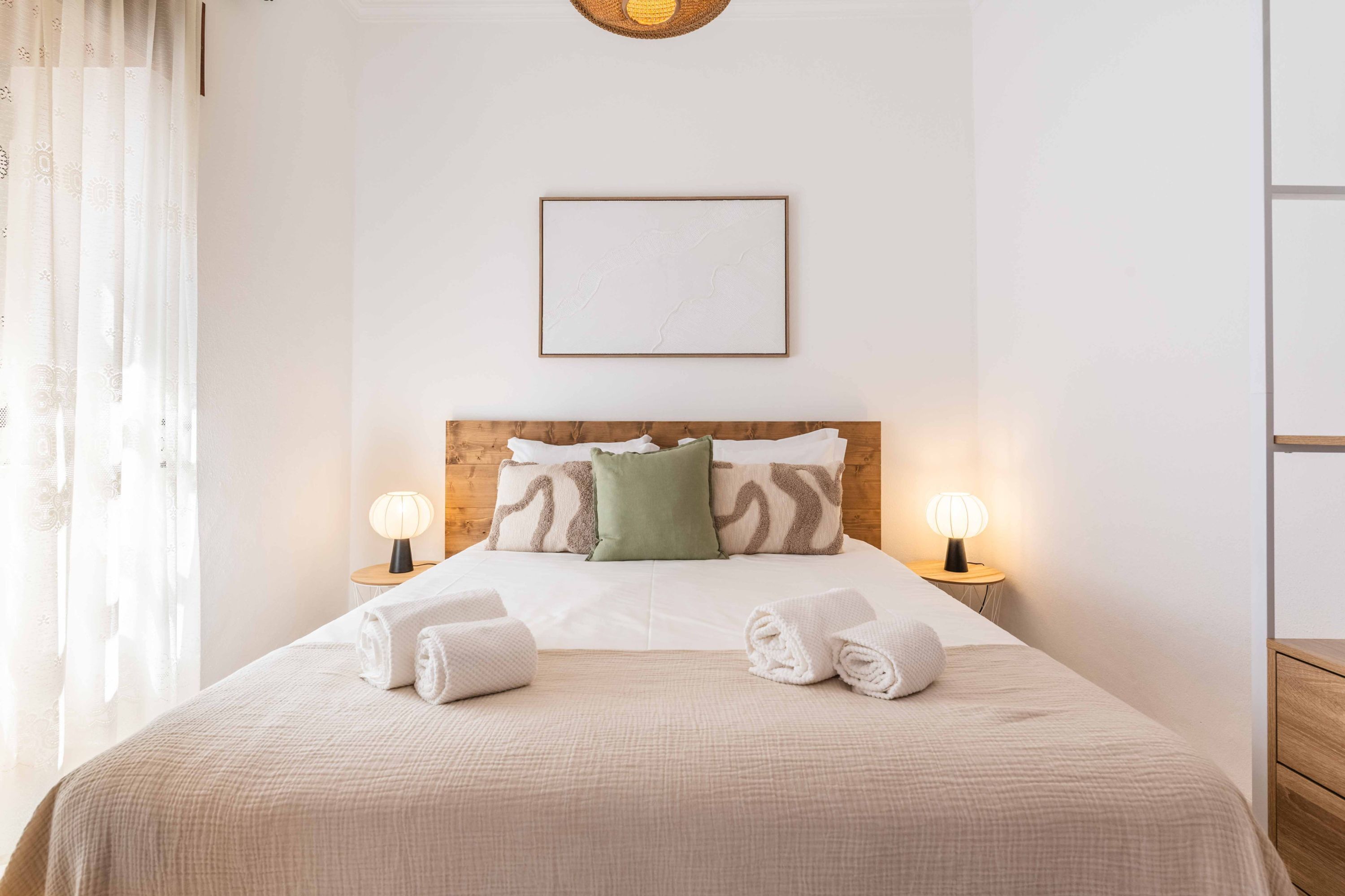 A neatly made bed with two pillows, two bedside lamps, and a framed picture on the wall.
