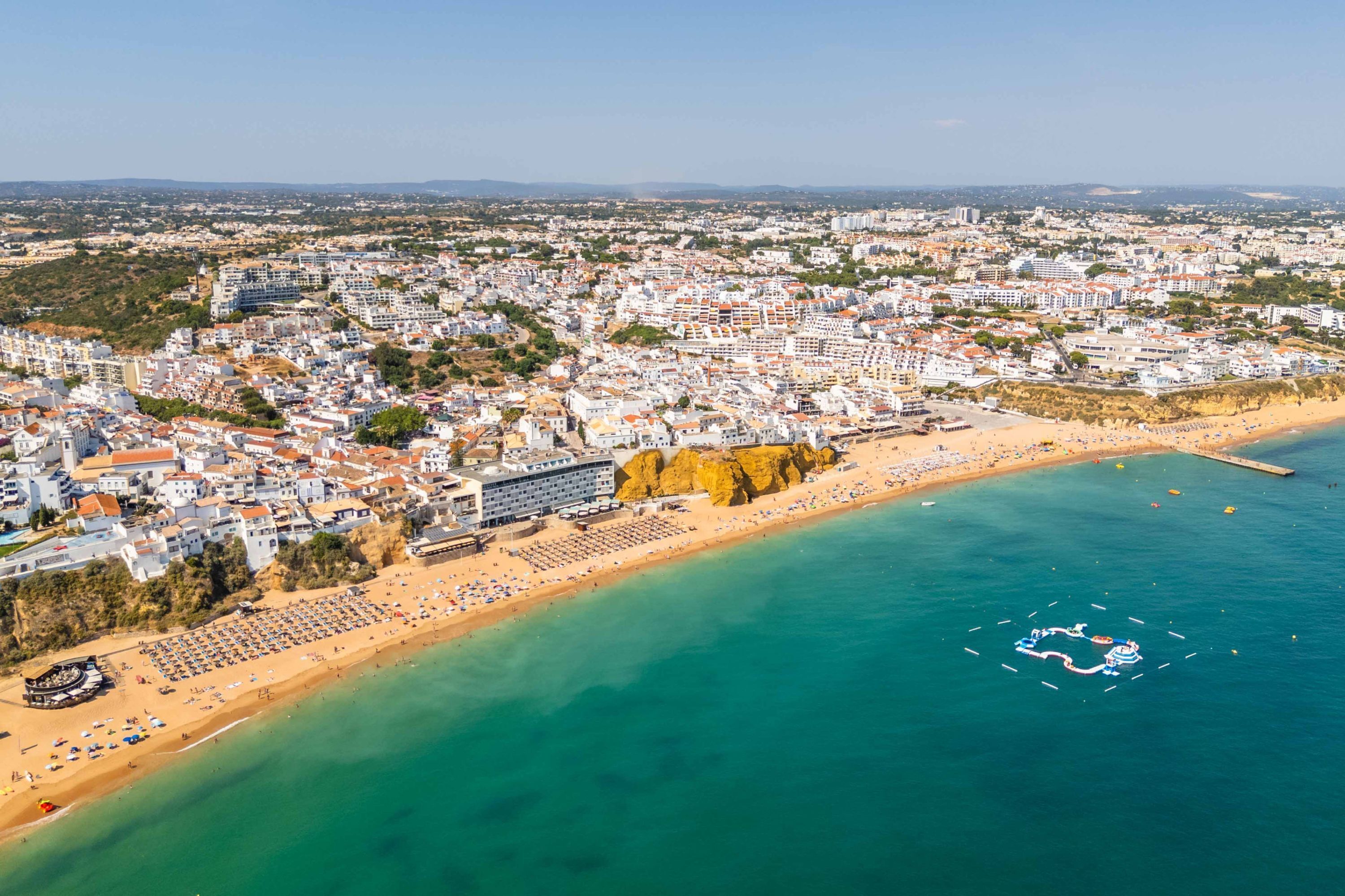 An aerial view of a coastal city with a beach, buildings, and a clear sky.