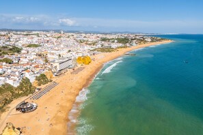 An aerial view of a coastal city with a sandy beach, a marina, and buildings along the shore. - Apartamento T1 Vistamar Centro Hist Rico Albufeira (Albufeira)