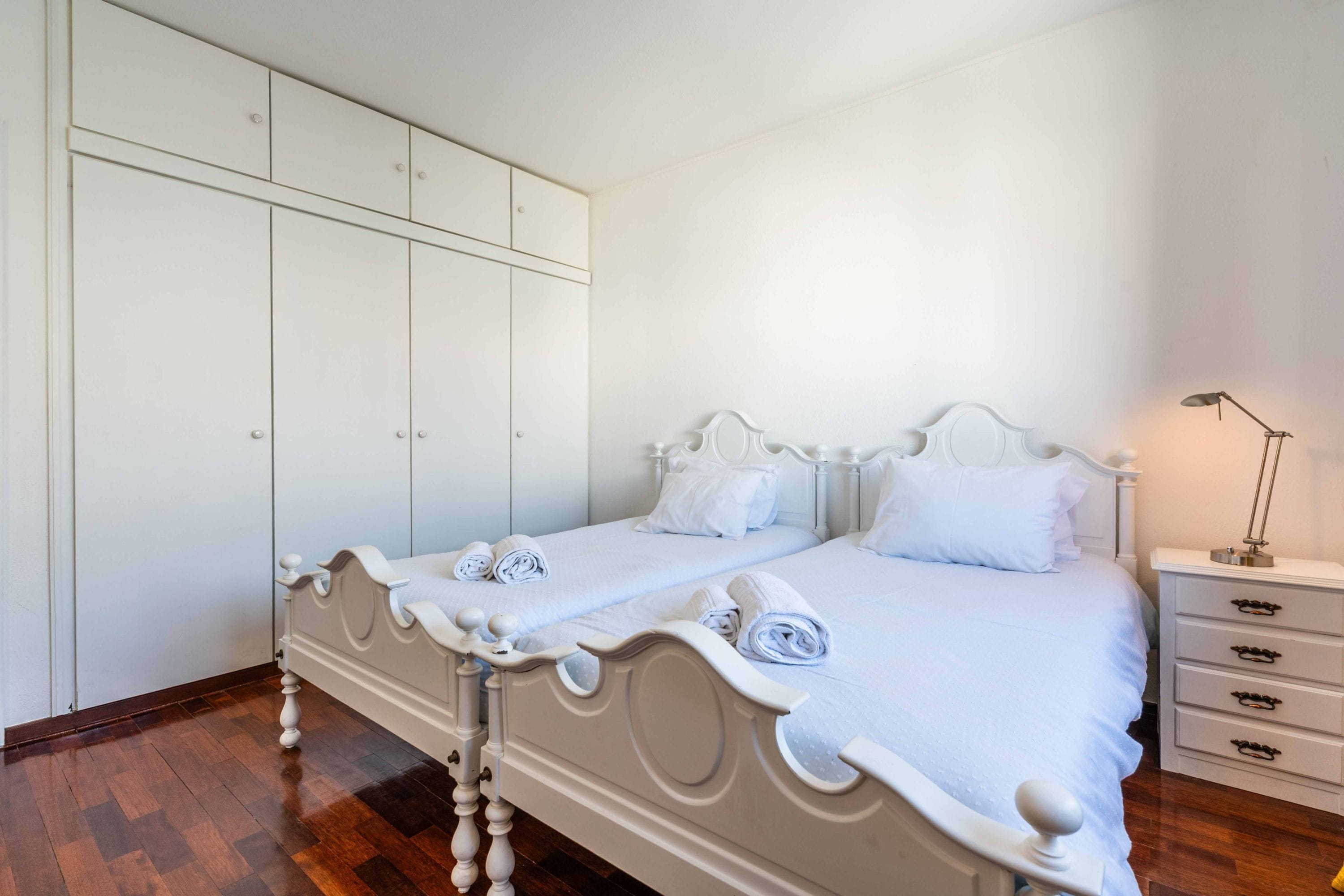 A double bed with a classic design, a bedside table with a lamp, and a wardrobe with multiple compartments.