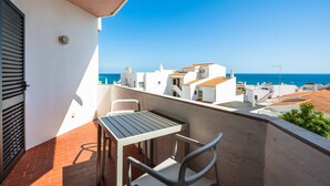 A balcony with a table and chairs, overlooking a coastal town with white buildings and a clear blue sky. - Apartamento T1 Vistamar Centro Hist Rico Albufeira (Albufeira)
