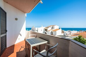 A balcony with a table and chairs, overlooking a coastal town with white buildings and a clear blue sky. - Apartamento T1 Vistamar Centro Hist Rico Albufeira (Albufeira)