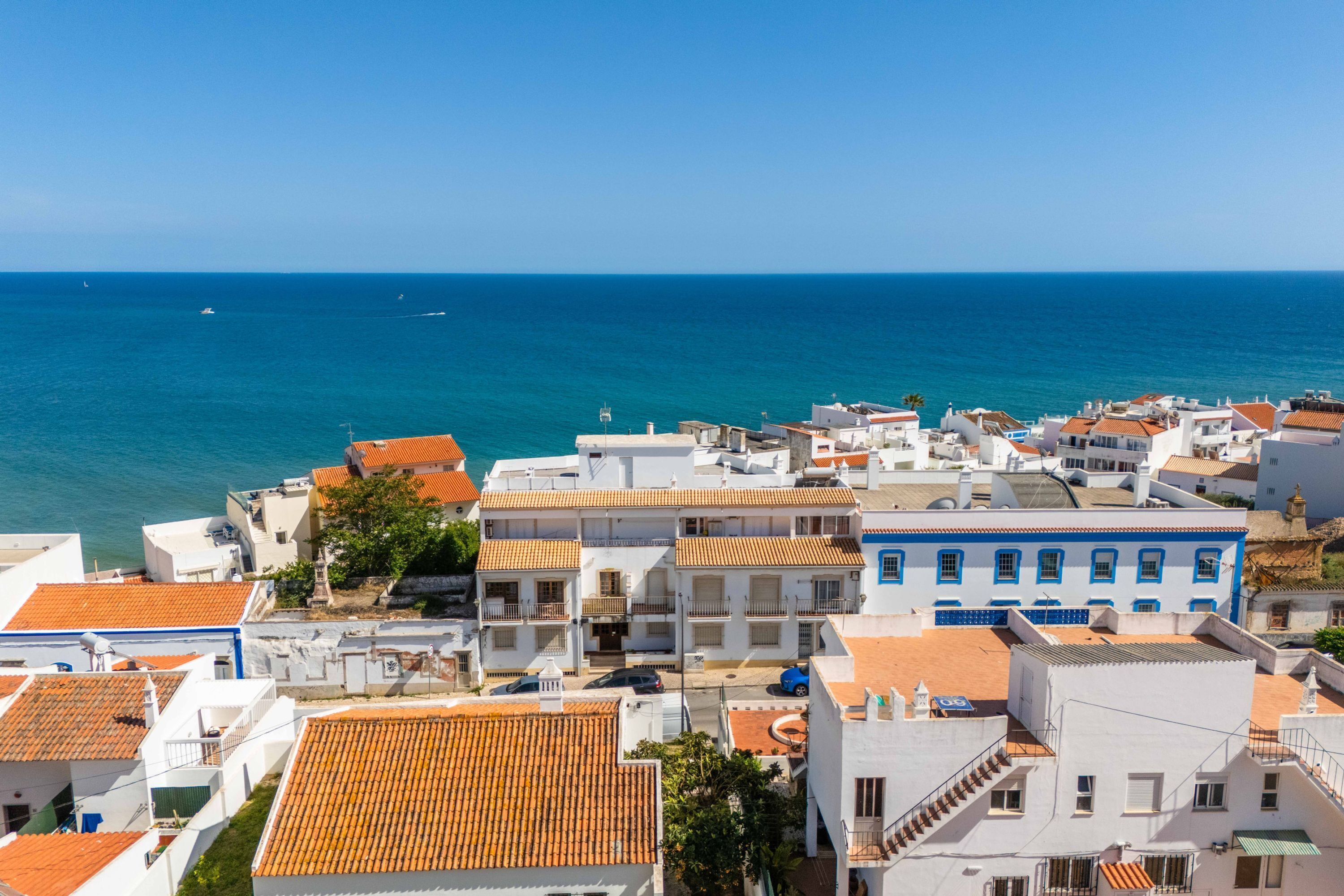 Eine Küstenstadt mit weißen Gebäuden und orangen Dächern, blaues, klares Meer und einige Boote in der Ferne.