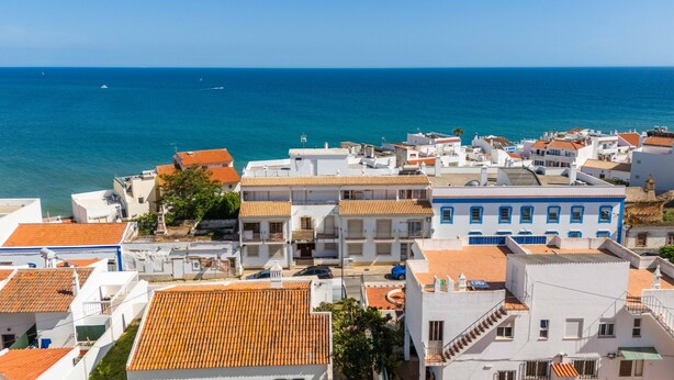 A coastal town with white buildings and orange roofs, a clear blue sea, and a few boats in the distance. - Apartamento T1 Vistamar Centro Hist Rico Albufeira (Albufeira)