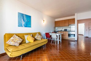 A living room with a sofa, a dining table with chairs, a kitchen area with cabinets and appliances, and a tiled floor. - Apartamento T1 Vistamar Centro Hist Rico Albufeira (Albufeira)