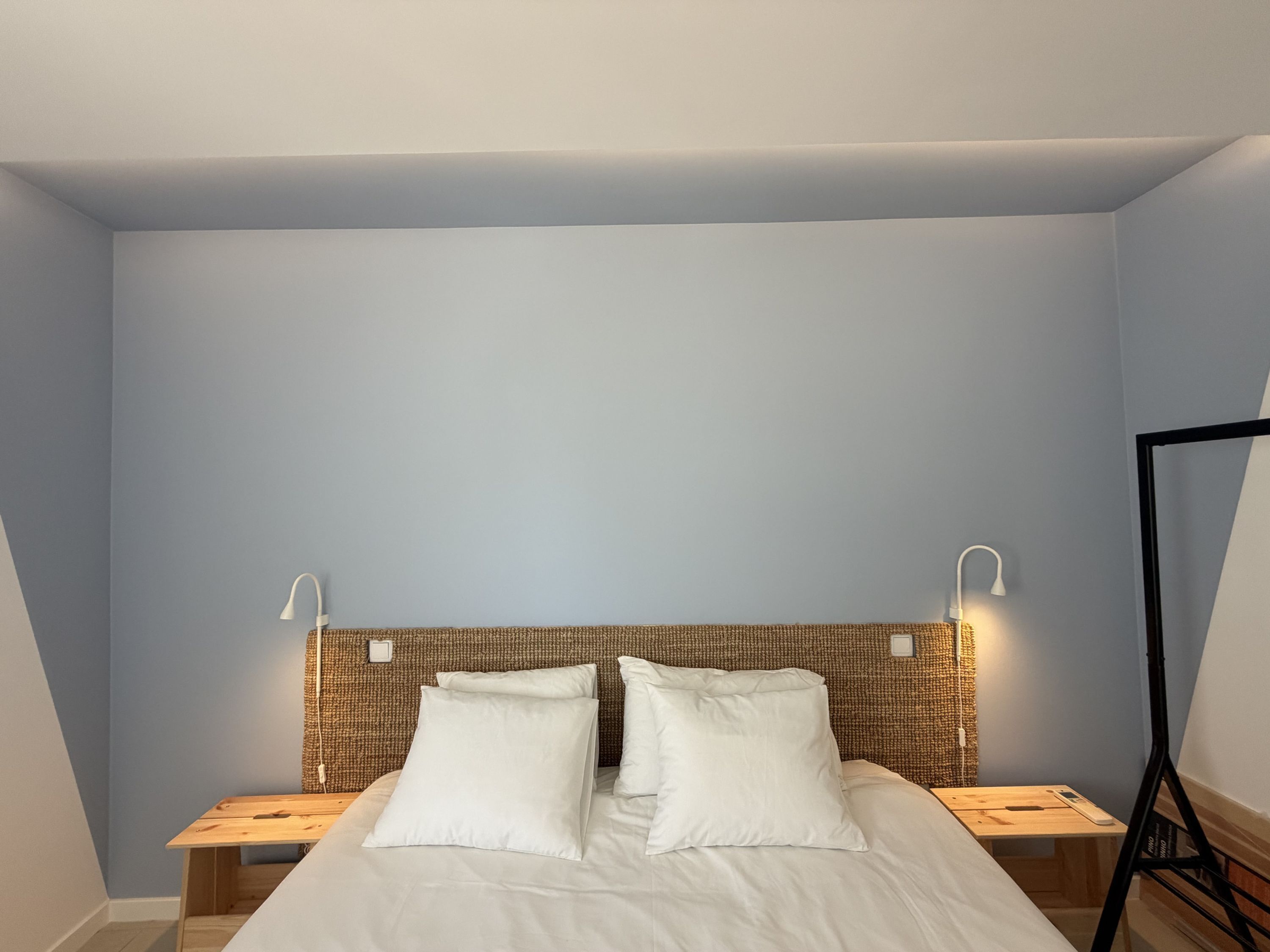 Ein Schlafzimmer mit einem Bett, zwei Nachttischen, einem Kopfteil mit gewebtem Muster und Wandleuchten zum Lesen.