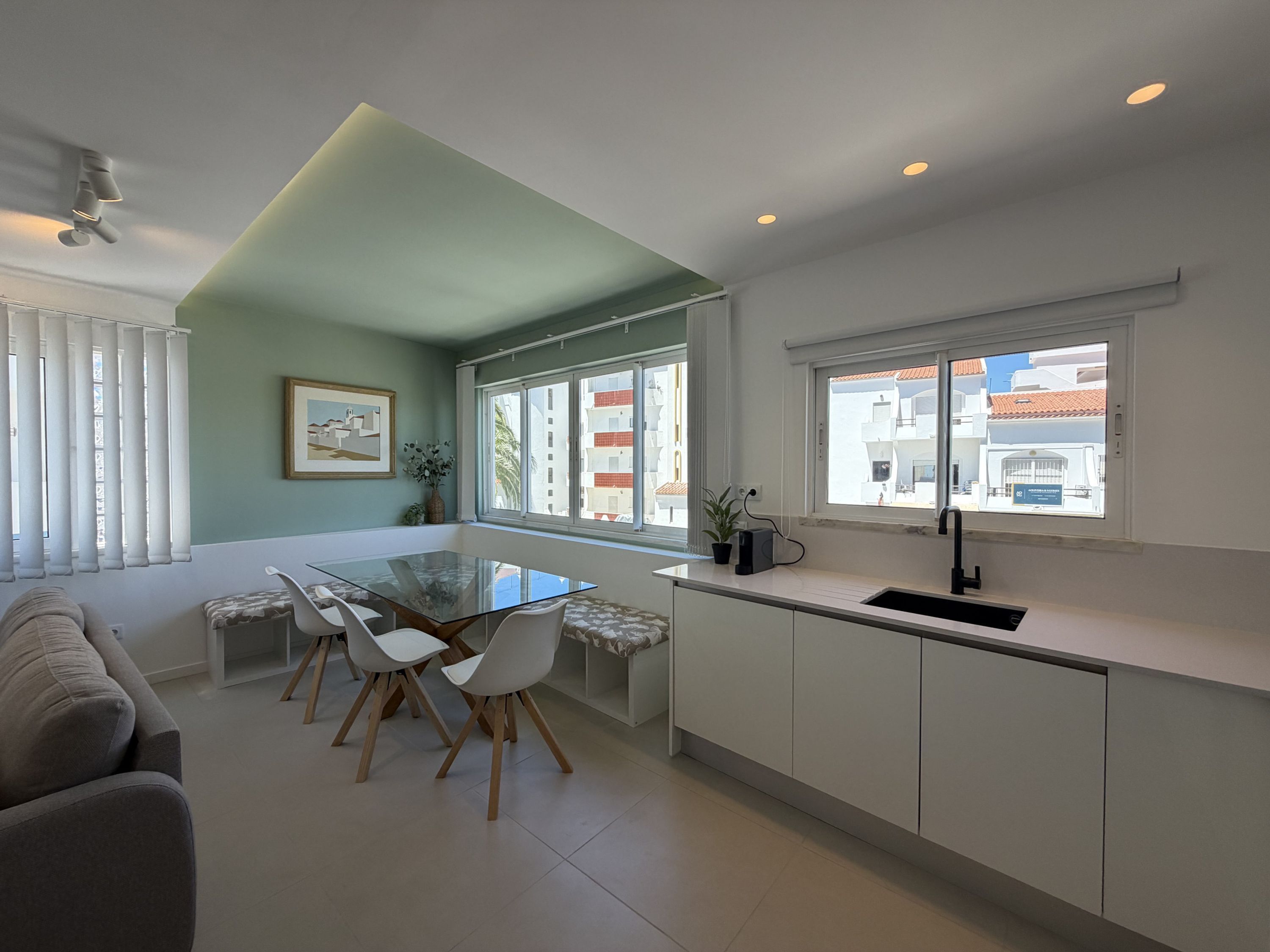 Una cocina moderna con una mesa de comedor de vidrio, armarios blancos y vistas de la ciudad a través de amplias ventanas.